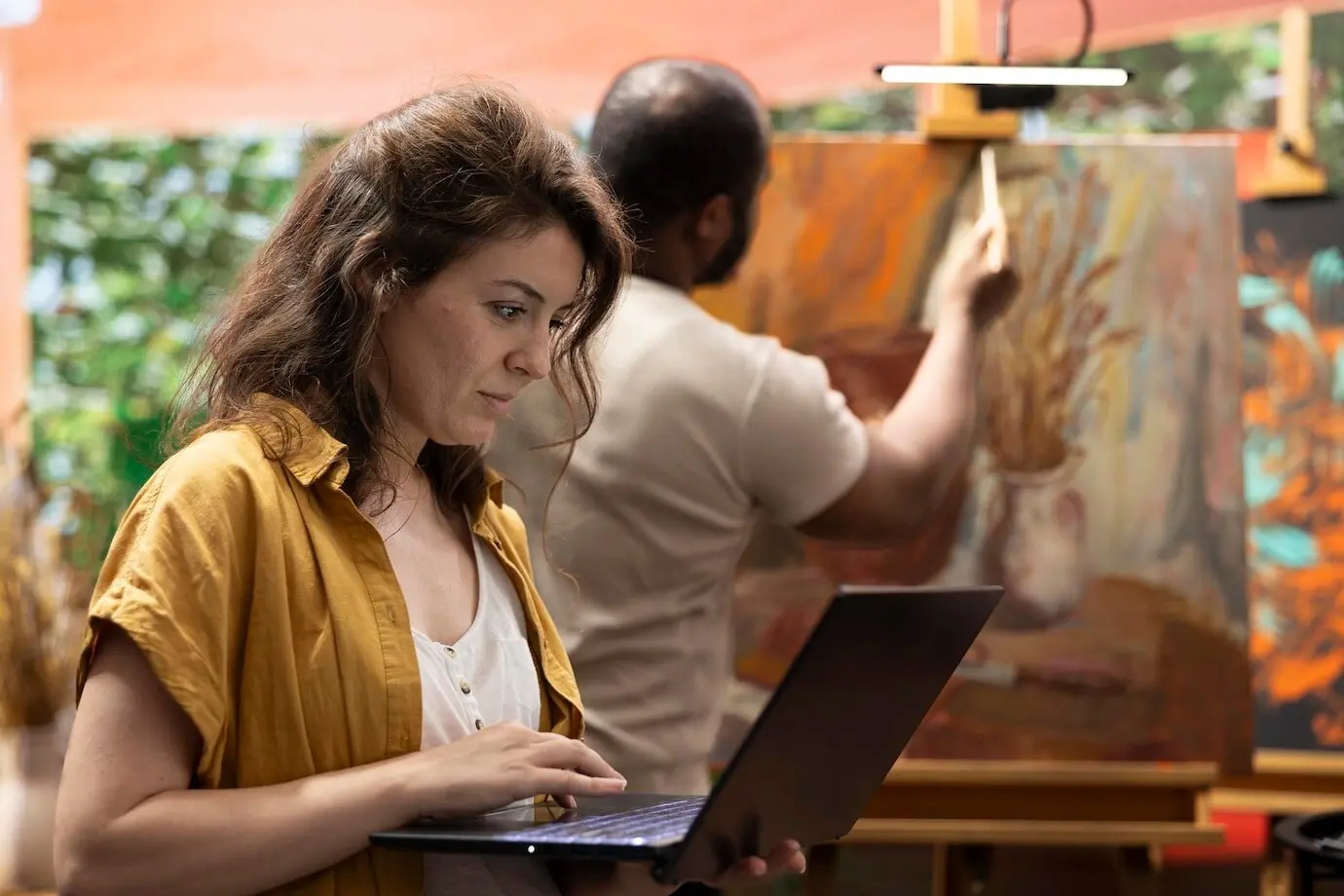 Una mujer busca inspiración en línea mientras un hombre pinta una obra maestra.